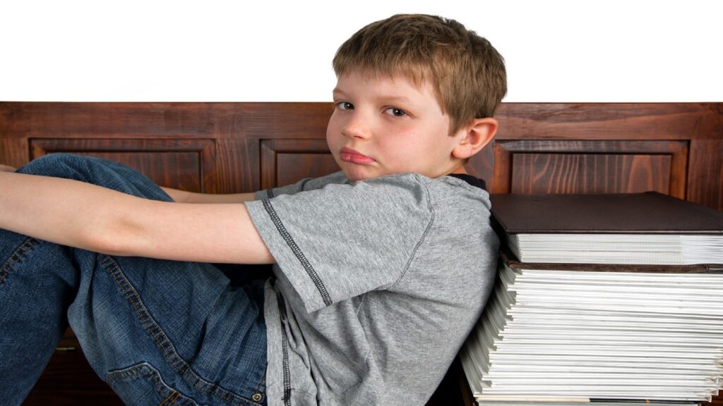 imagem para o artigo número de livros lidos por nossas crianças, mostra um menino triste encostado nos livros.